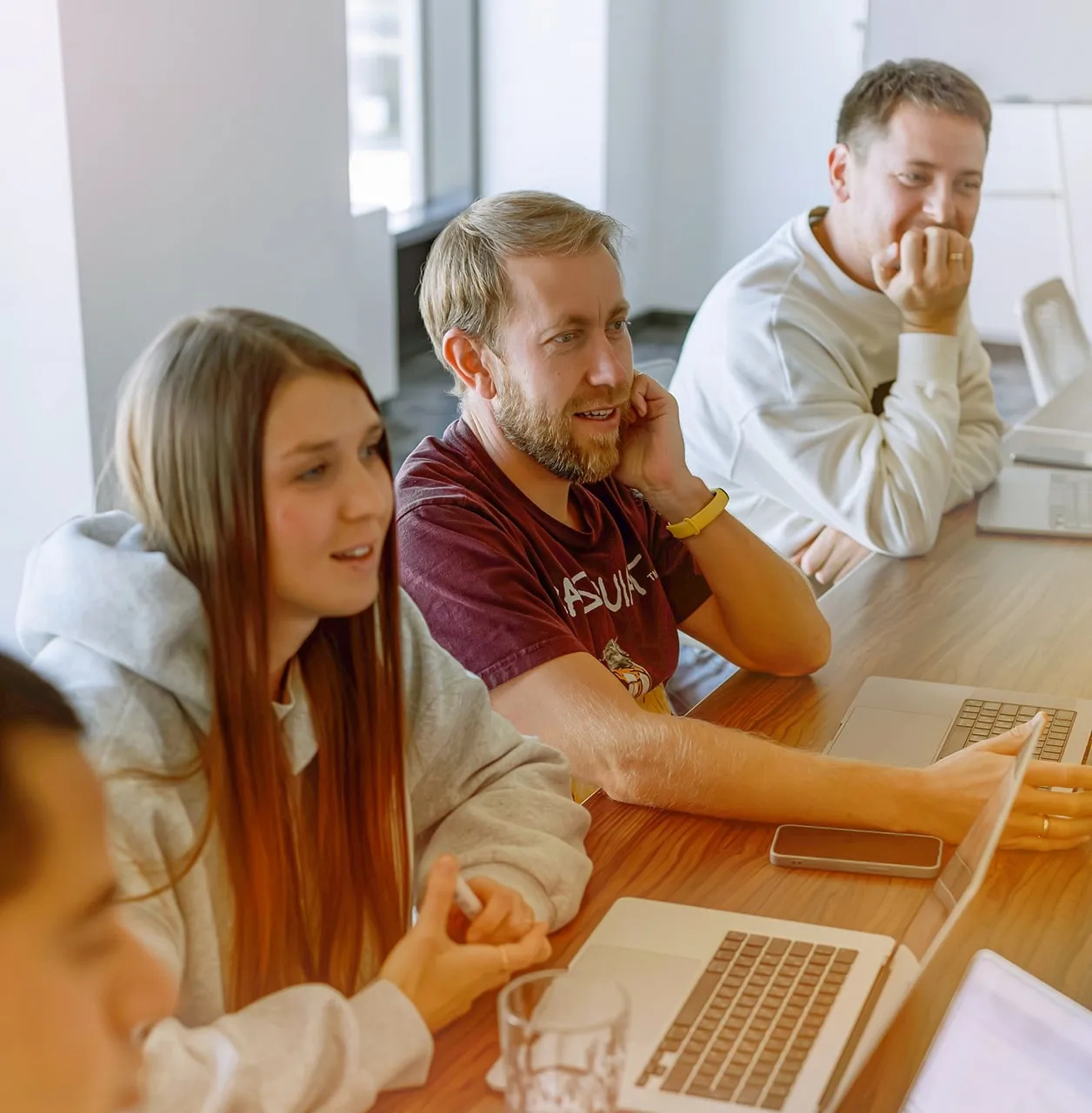 Group of people sitting at a table with laptops, engaged in discussion.
