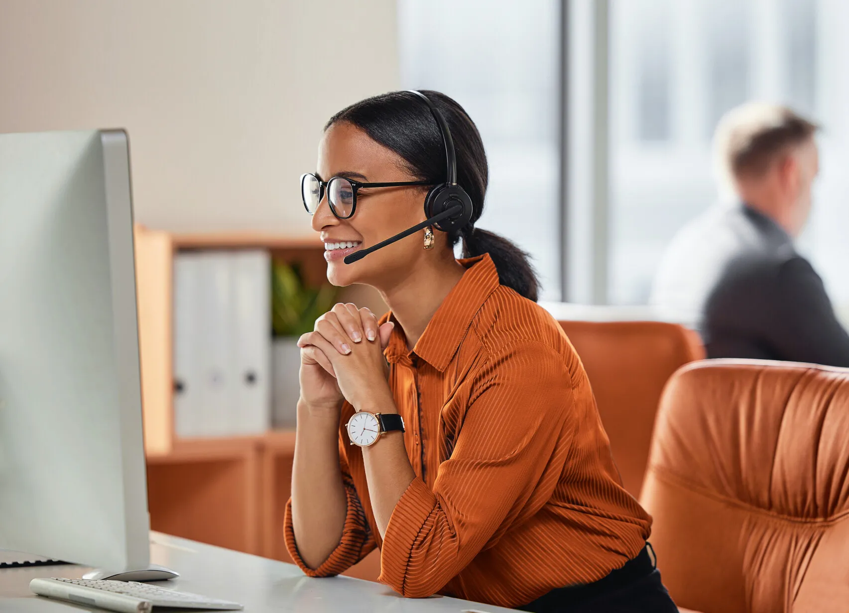 Smiling woman with headset on a VoIP business call from a bright home office.