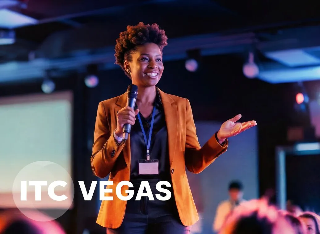 A speaker in a blazer holding a microphone on stage at ITC Vegas, engaging with the audience under colorful lights.