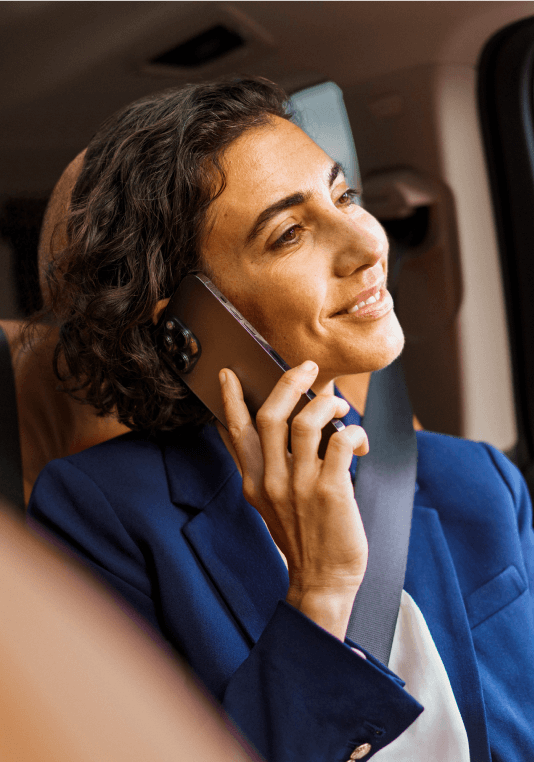 Una cliente que sonríe mientras sostiene su teléfono móvil en un coche