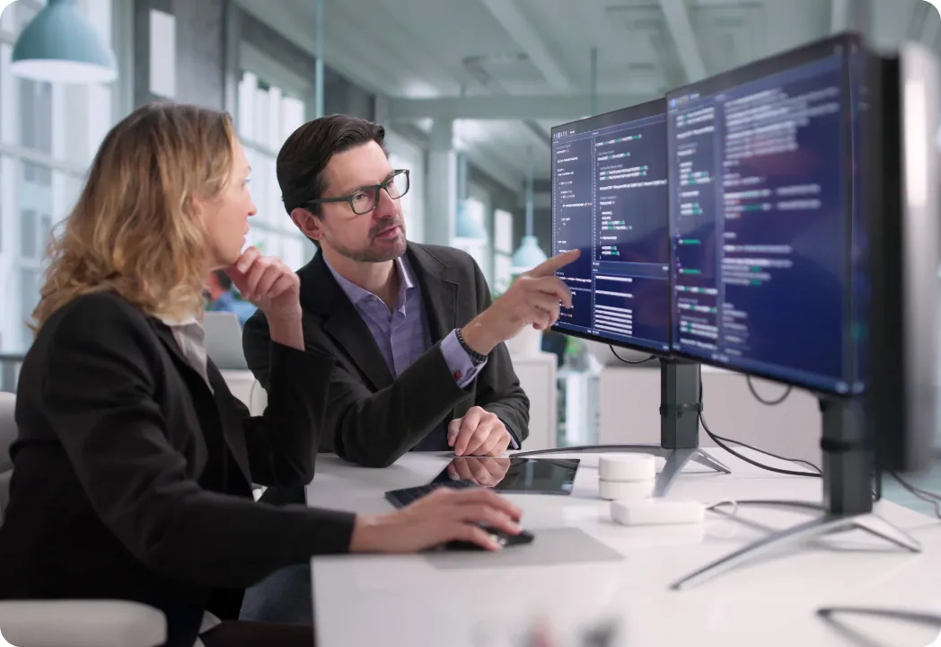 Two individuals looking at a computer screen, appearing to share insights or work together on a task.