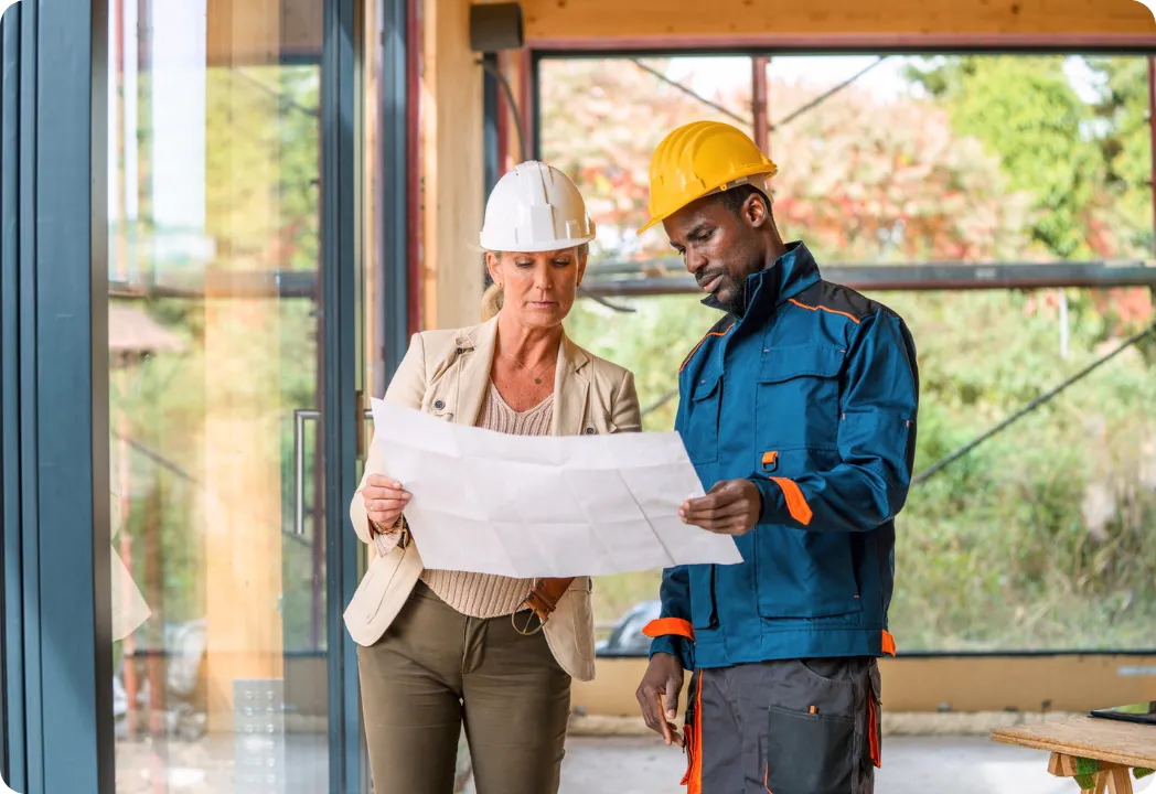 Two individuals in hard hats examining a blueprint at a construction site, discussing plans and details.