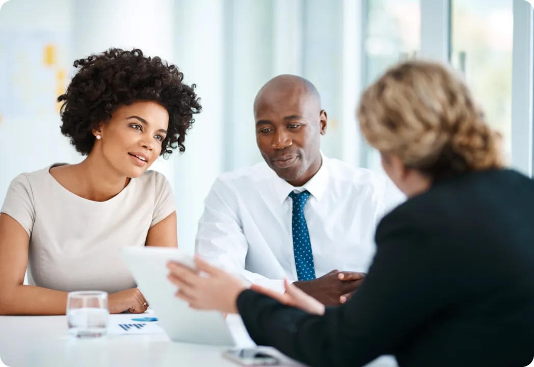 Three business professionals seated at a table, collaborating over a laptop during a meeting.