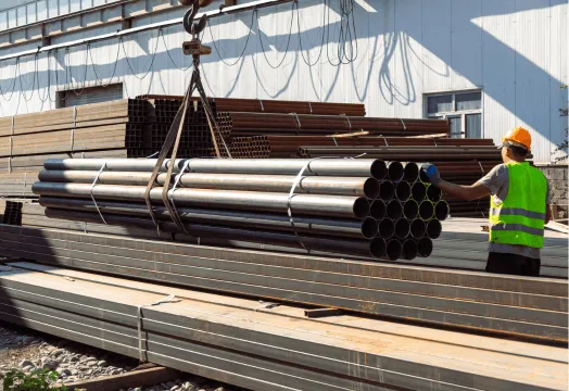 A man stands beside a large pile of steel pipes, showcasing industrial materials in a construction setting