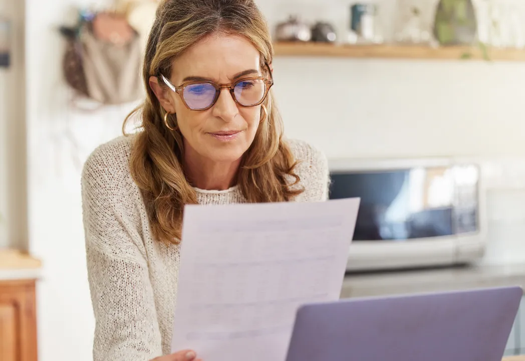 A woman wearing glasses is focused on a document displayed on her laptop screen.