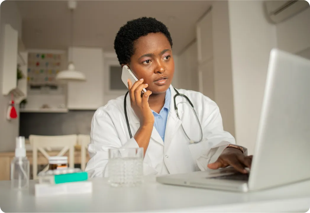 A female doctor is speaking on the phone and using a laptop