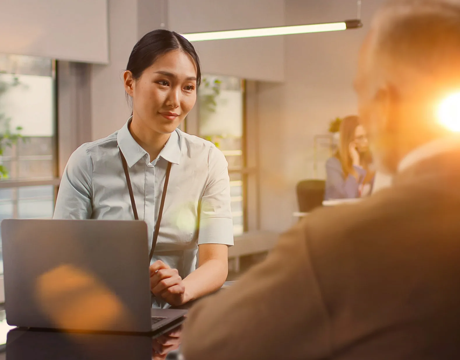 A woman in front of a laptop is assisting a customer across the table