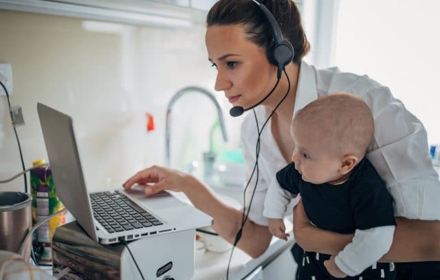 mother working in kitchen on laptop and holding her baby