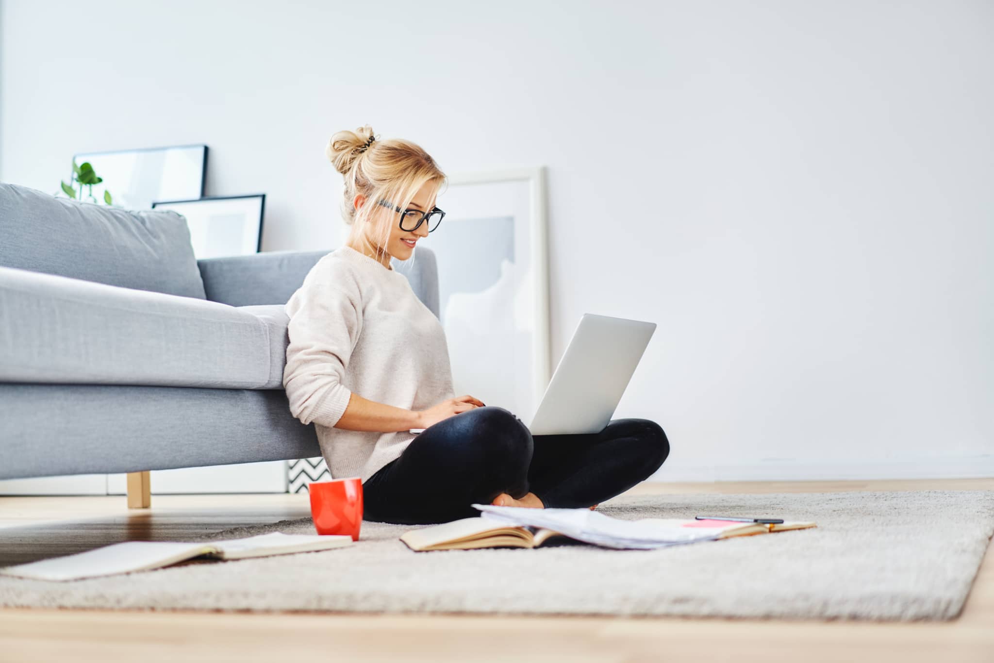 Woman sitting on floor of her apartment with laptop and notes working