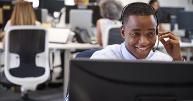 Young man working at computer with headset in busy local council office