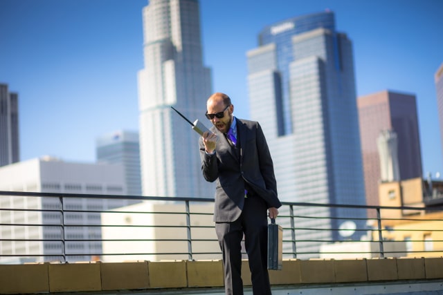 Amanposesontheroofofanofficebuildingwithamobiletelephonefromthesorearlys.