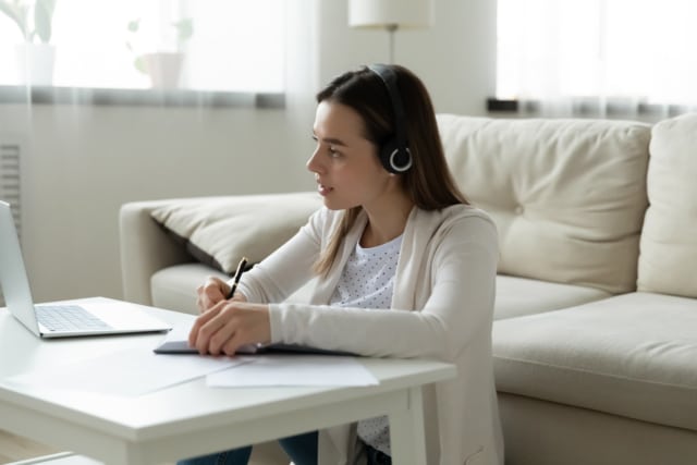 focused woman in headphones watch webinar on laptop writing notes