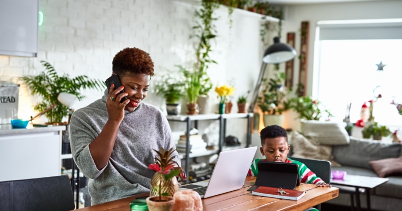 woman smiling on the phone to customer service while working at home with her son