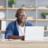 Hotline support service. African american male call center operator in headset working with laptop computer at home
