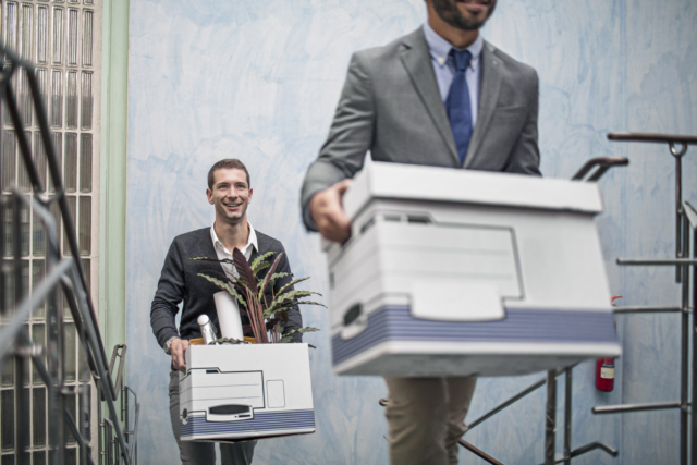 Businessman smiling while carrying belongings on staircase with coworker. They are moving up to a new office.