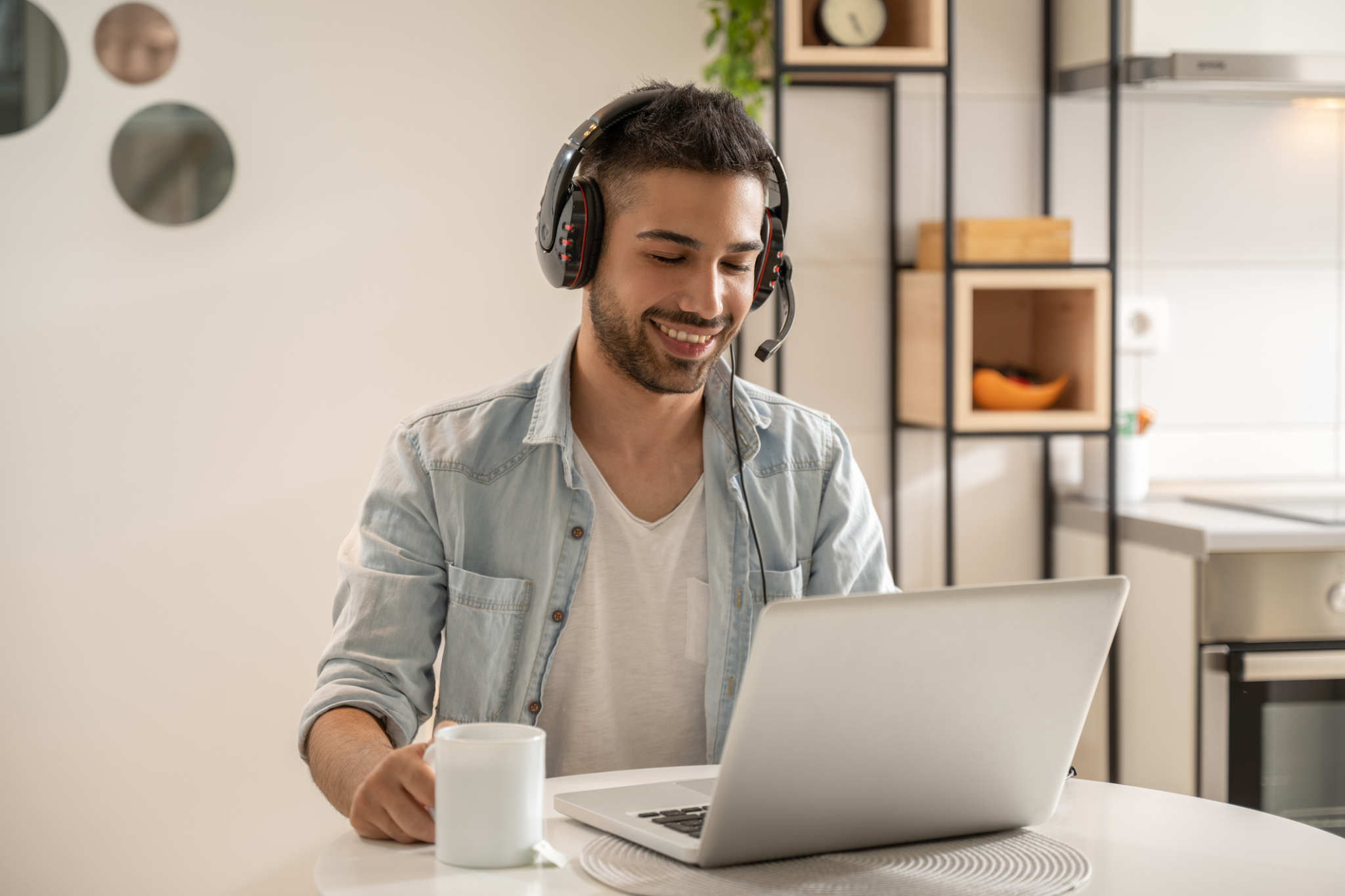 Portrait of smiling man wearing headphones with microphone using laptop at home.-817