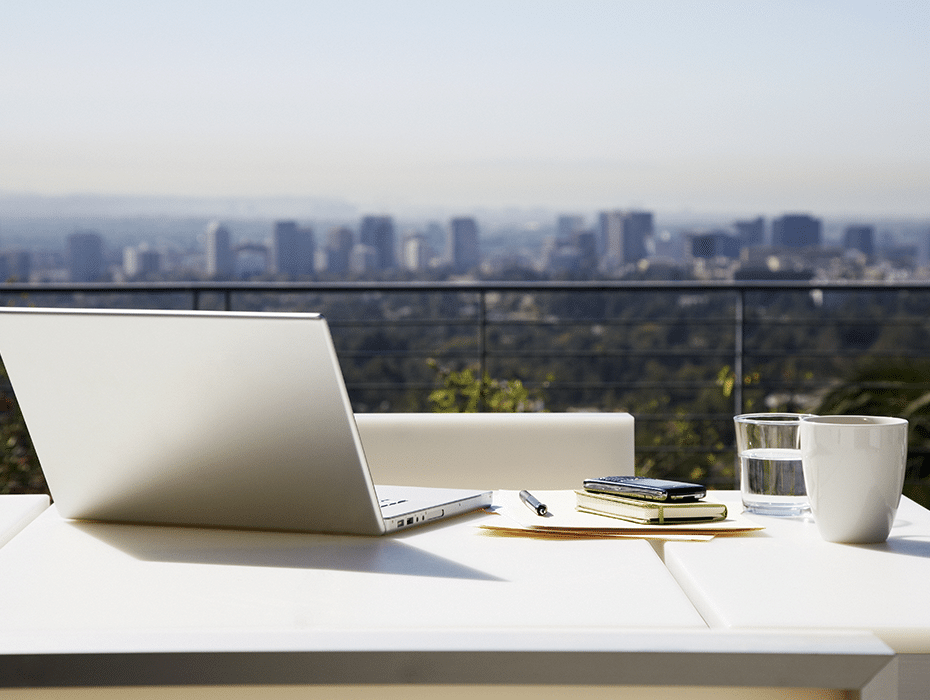 Computer on desk outside with a beutiful landscape of a city with trees in the background