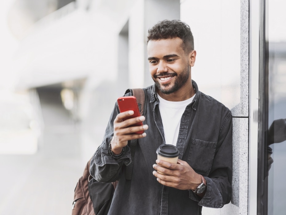 Young handsome men using smartphone in a city. Smiling student man texting on his mobile phone. Coffee break. Modern lifestyle, connection, business concept