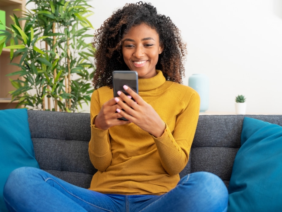 Confident black woman scrolling on smartphone at home