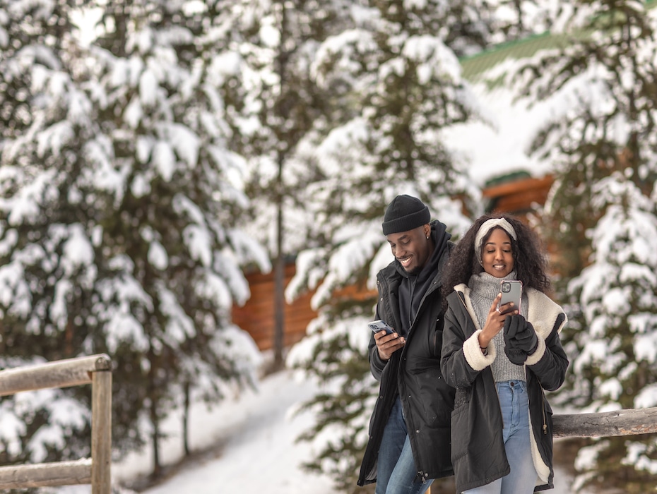Couple walking through snowy trees checking their phones