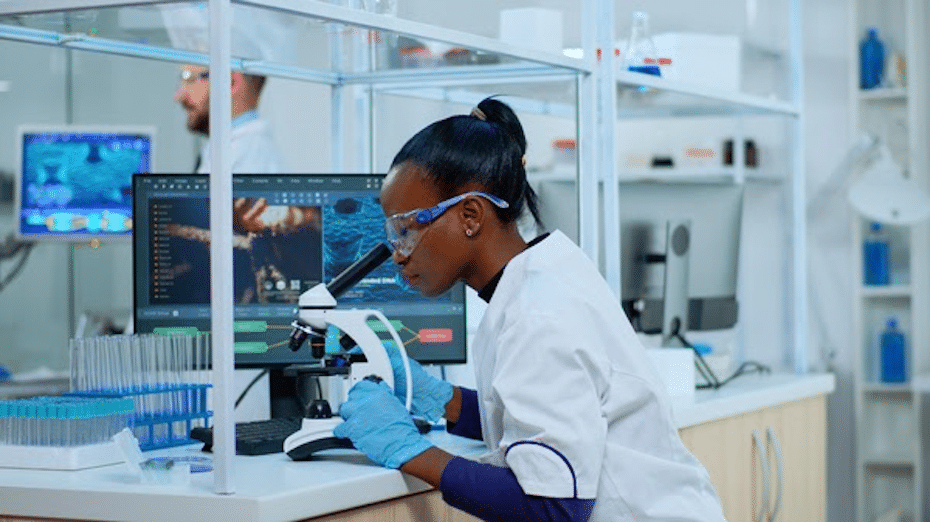 African-American female research scientist looks through microscope in R&D laboratory