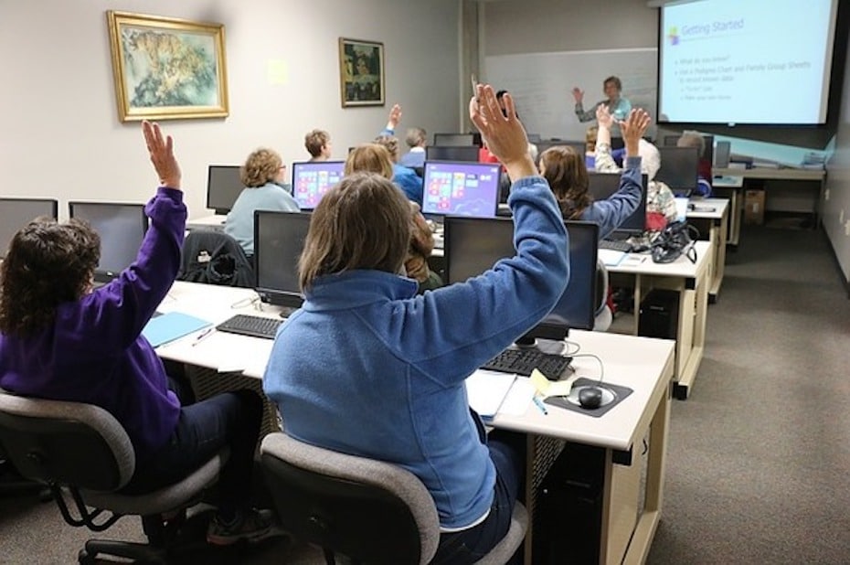 Adult students with hands raised in a classroom setting