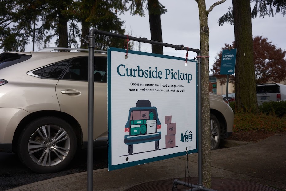A car sits idly next to a sign that says "Curbside Pickup"
