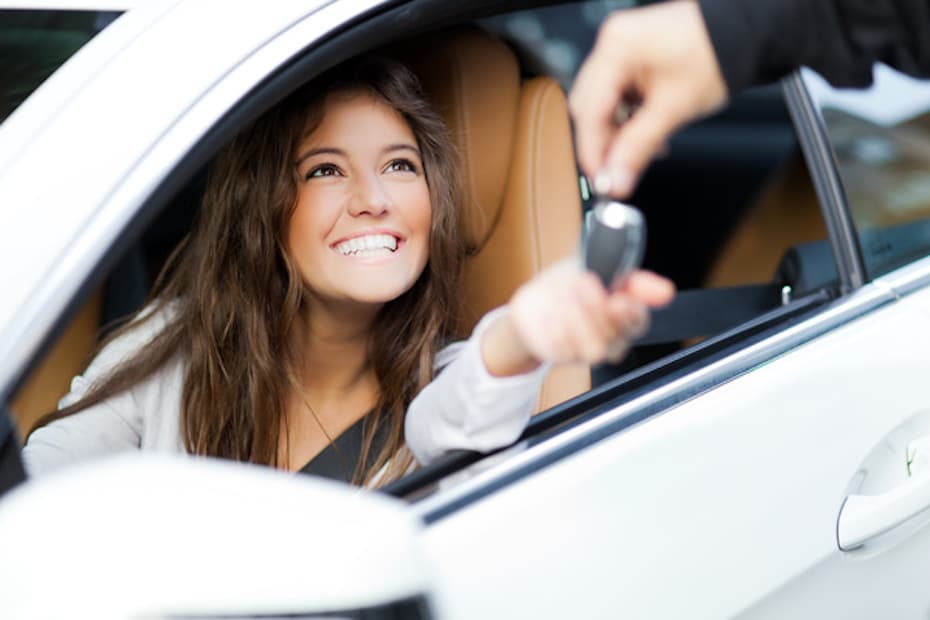 Young female insurance customer, smiling in the driver's seat of a new car, with her hand outreached for the keys