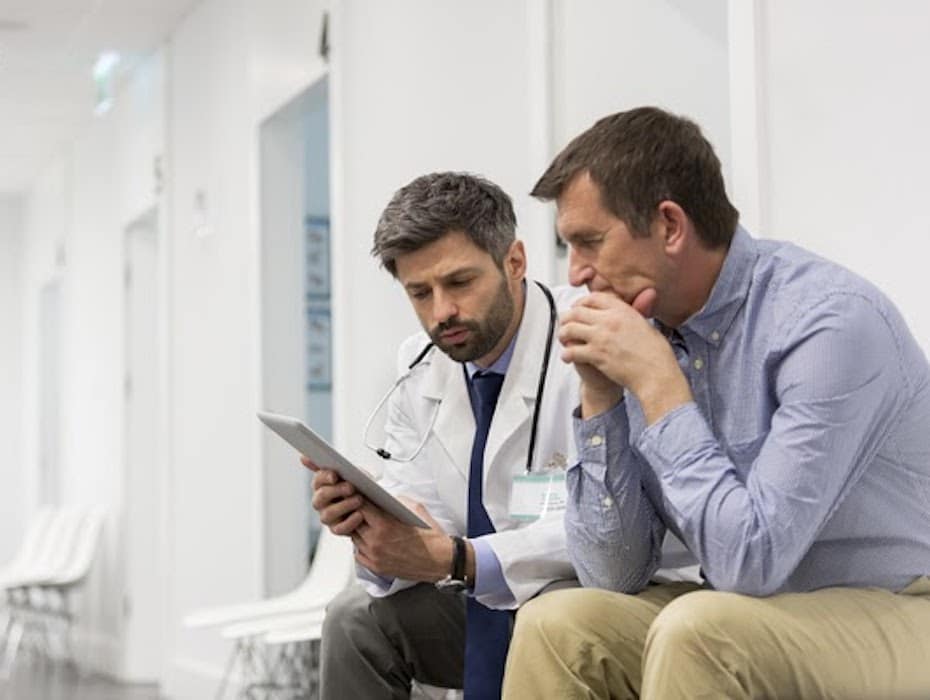 A doctor and a patient review medical paperwork together in a hospital setting.