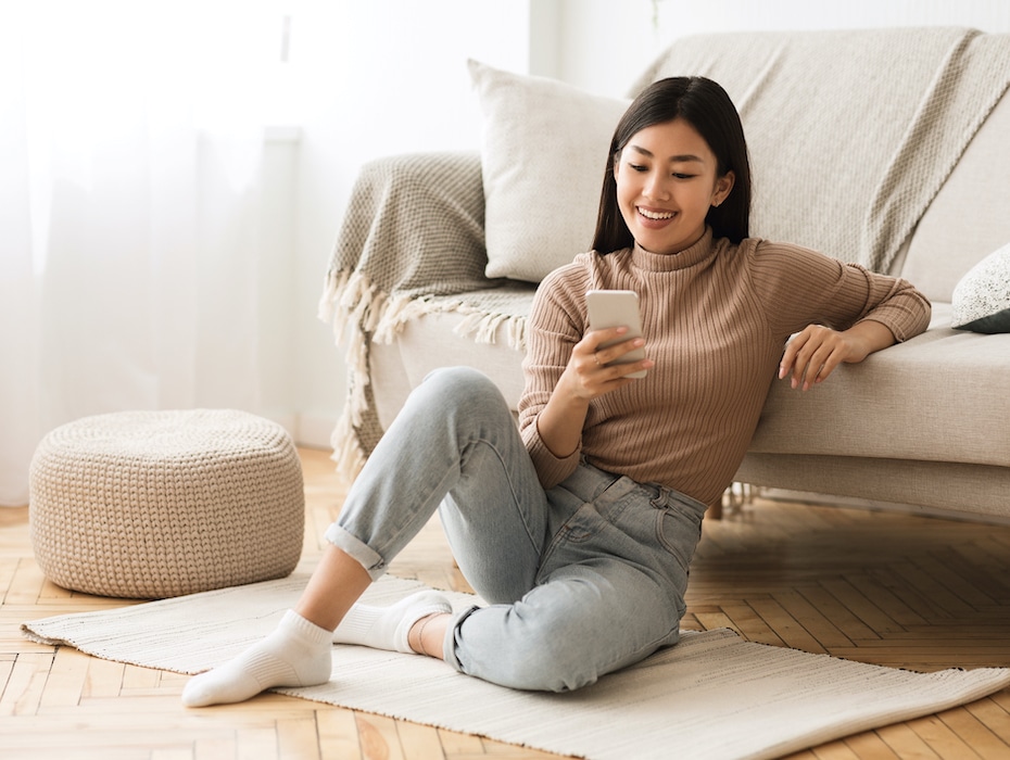 Person messaging on phone at home, sitting on floor near sofa with communications tool