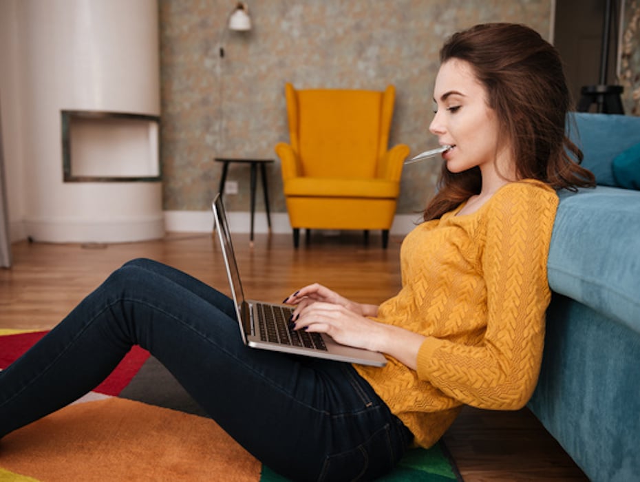 woman sits on floor leaning against sofa while performing online banking as a service on her laptop