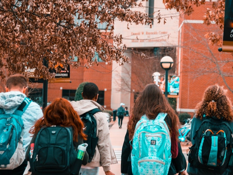 Students wearing backpacks outside at the bottom of the steps leading to an academic institution