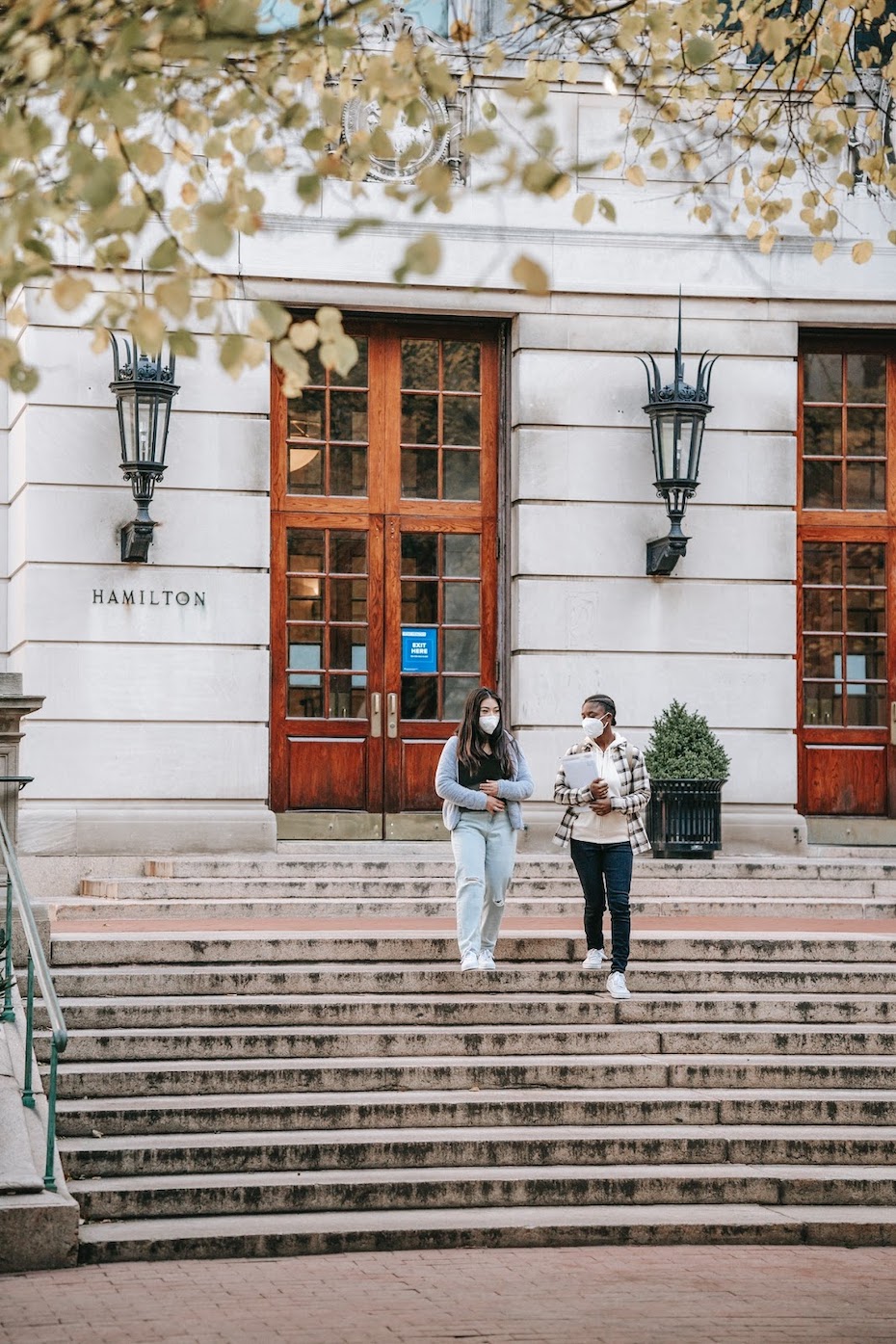 two students wearing masks walking down the steps in front of an academic institution during the COVID pandemic