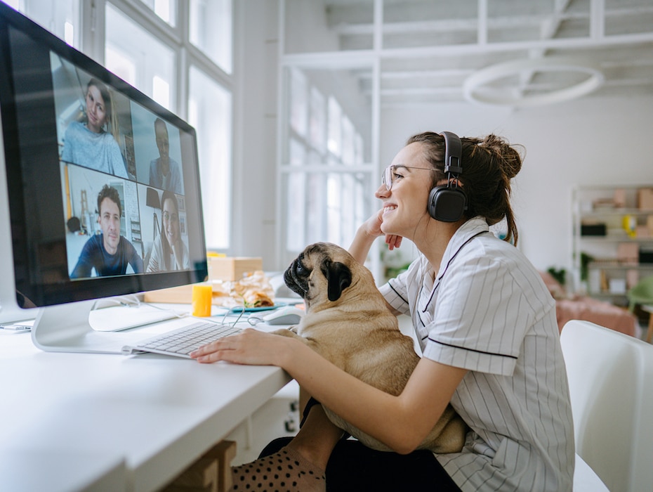 Photo of a smiling young woman having a video call, accompanied by her dog; the daily routine of a young woman working from home.