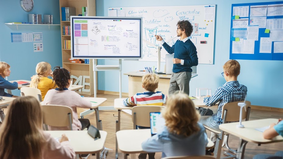 A teacher standing in front of the class teaching from a large board
