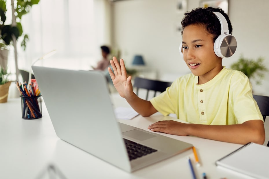 African American boy using laptop and waving during video call while homeschooling to demonstrate the benefits of video conferencing in education