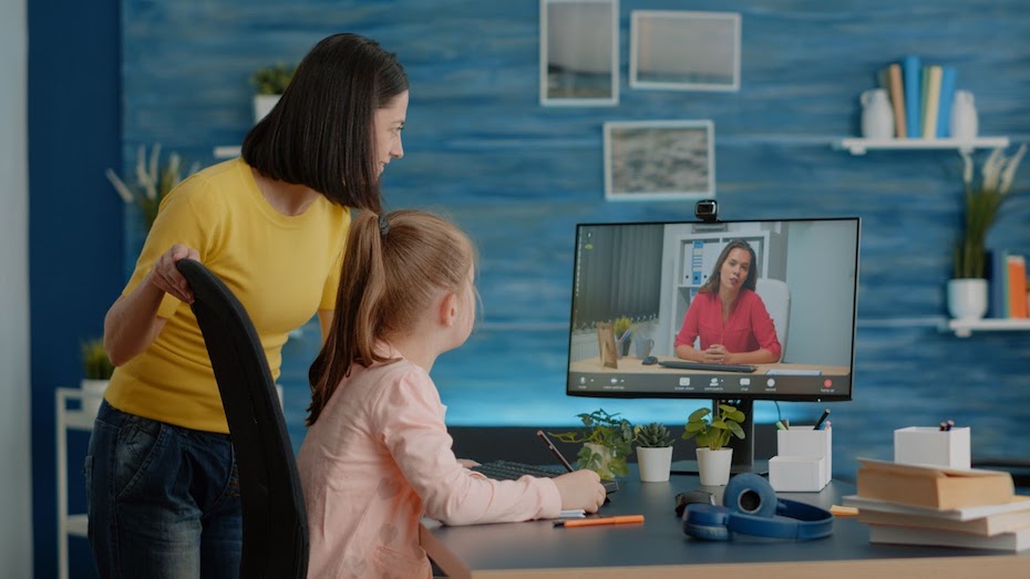 A student and her parent interact with a teacher via video conferencing while sitting at a desk