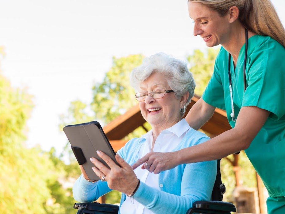 Nurse pushes elderly woman in wheelchair while she uses tablet