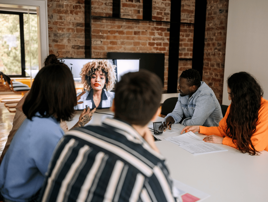 Multiracial group of teammates in a meeting room with video conferencing on TV