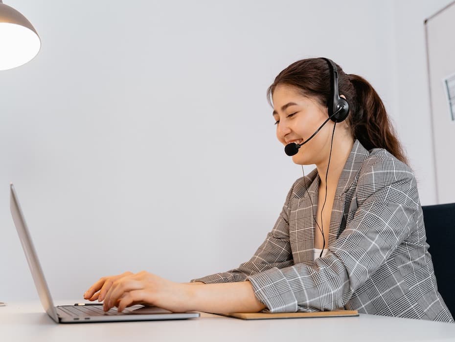 A smiling government contact center agent with headset delivers excellent citizen experience as she sits in front of her laptop