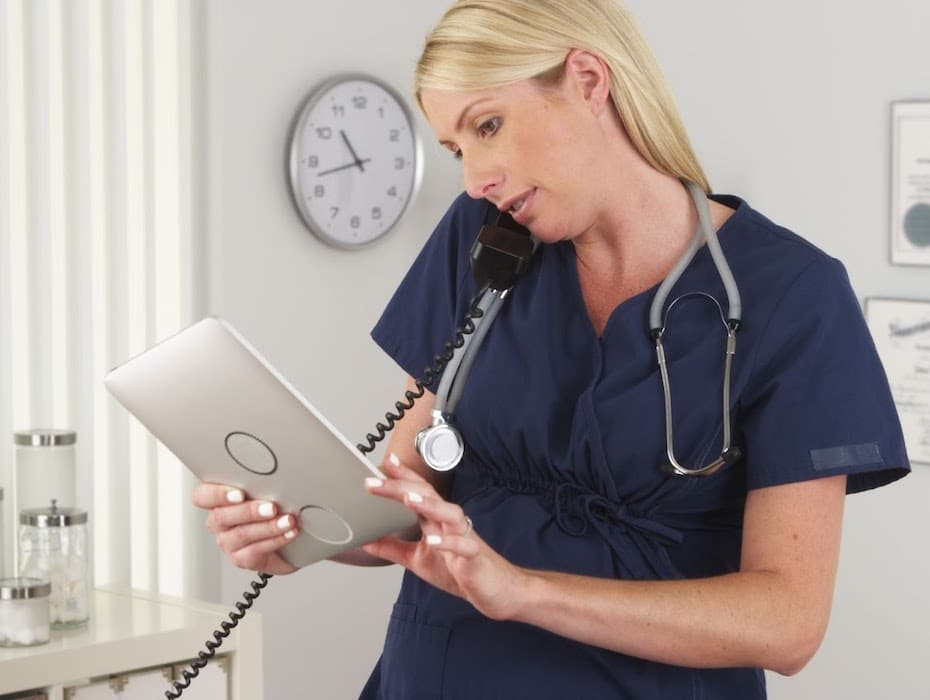 A healthcare provider juggles a phone and tablet to work on a prior authorization request.