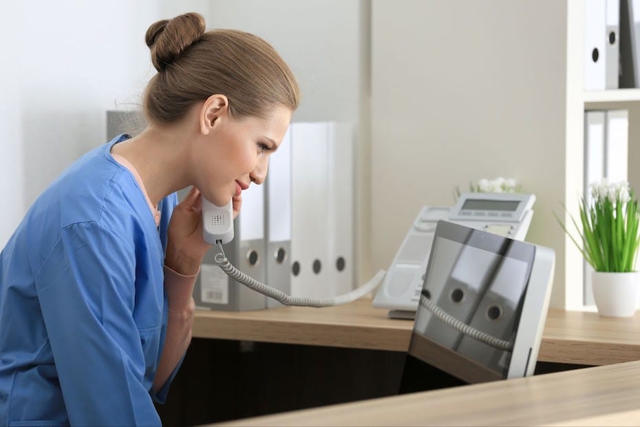 A healthcare provider sits at a desk on the phone with a tablet to submit a prior authorization request.