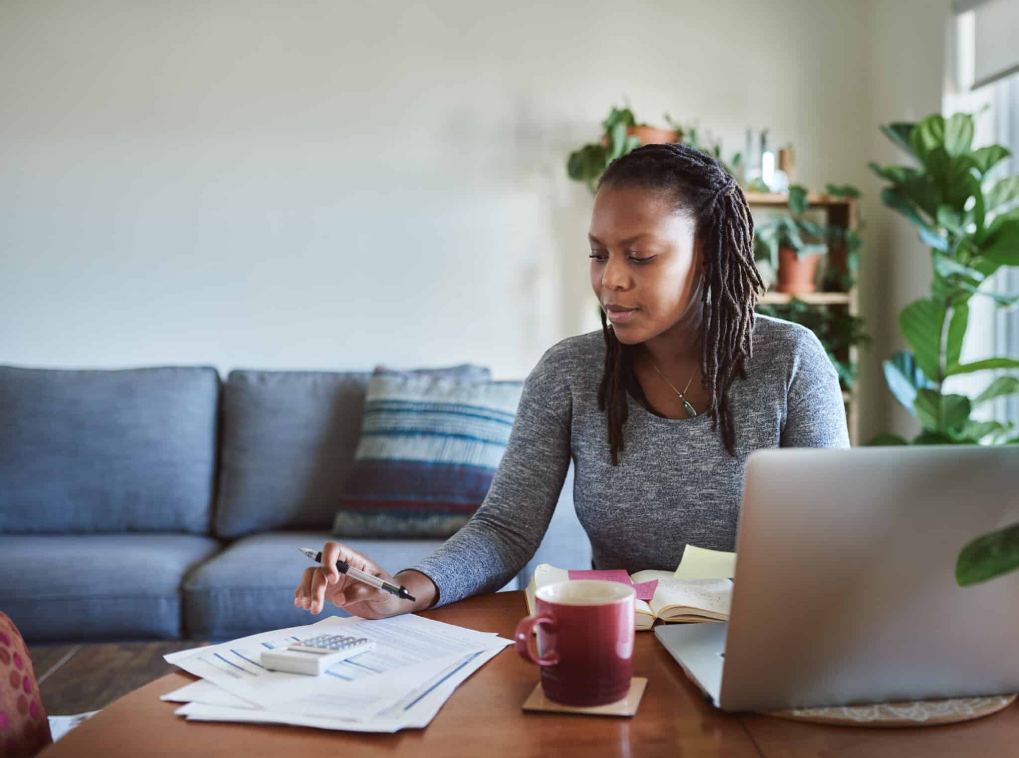 Shot of a young woman using a laptop and going through documents while working from home