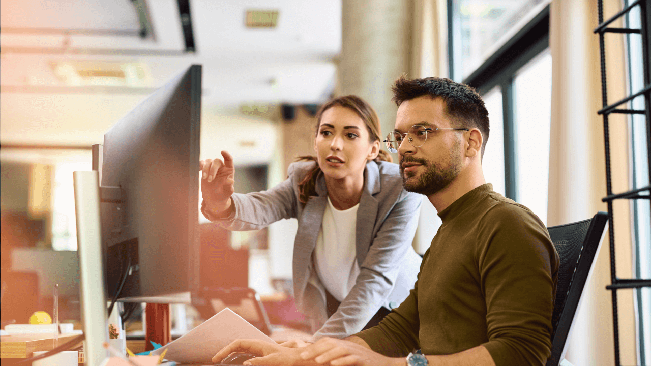 A man and woman collaborate on a computer, focused on their work in a modern office setting.