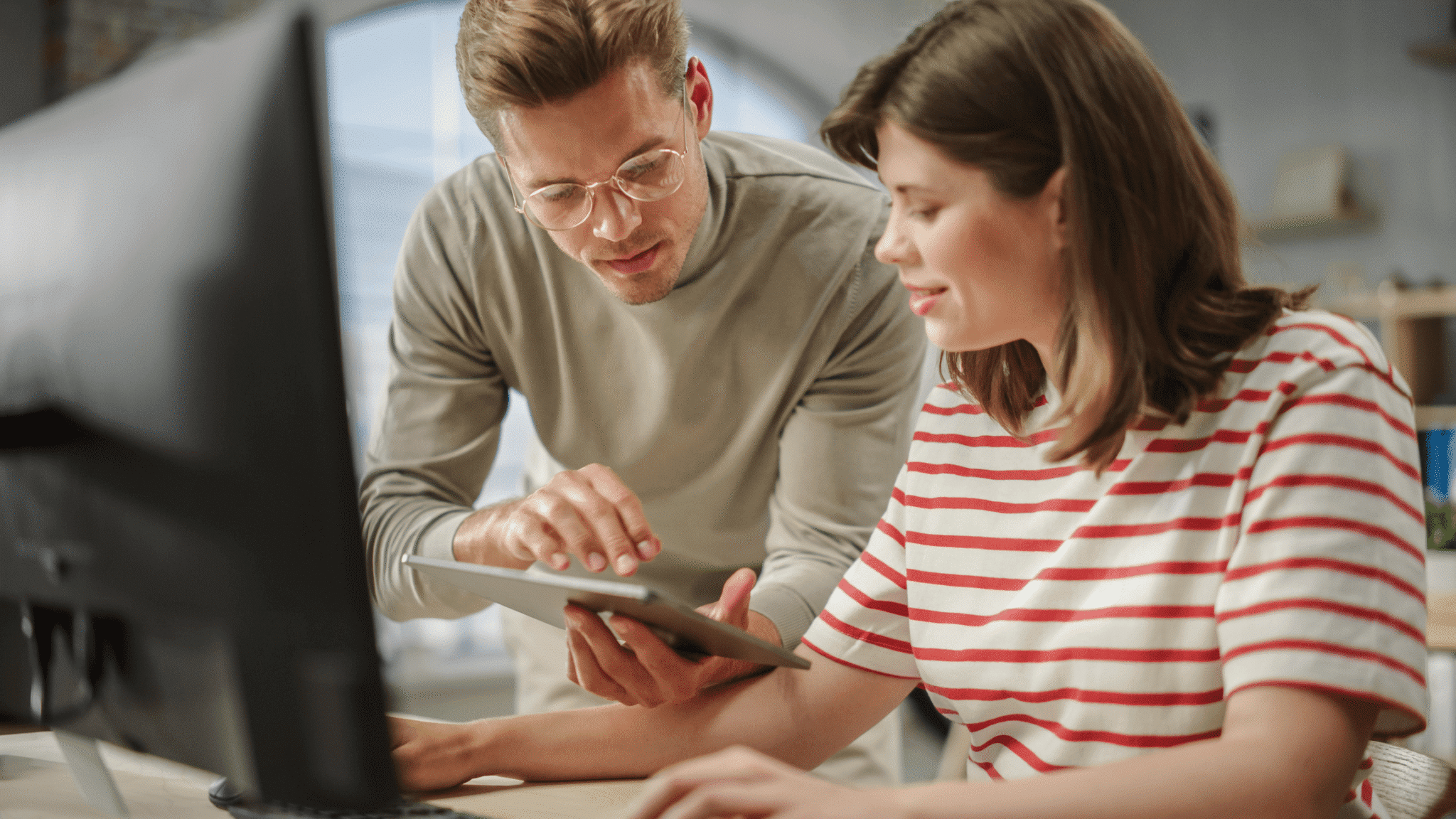 A man and woman are engaged in discussion while looking at a tablet computer together.