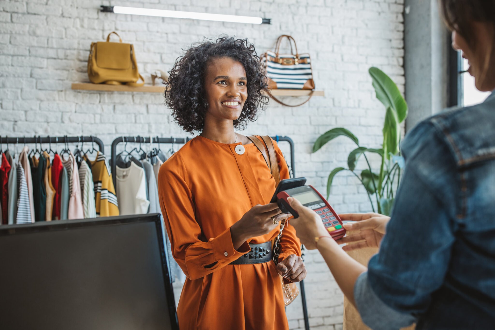 A customer in an orange dress is making a digital payment via her mobile phone in a clothing retail store