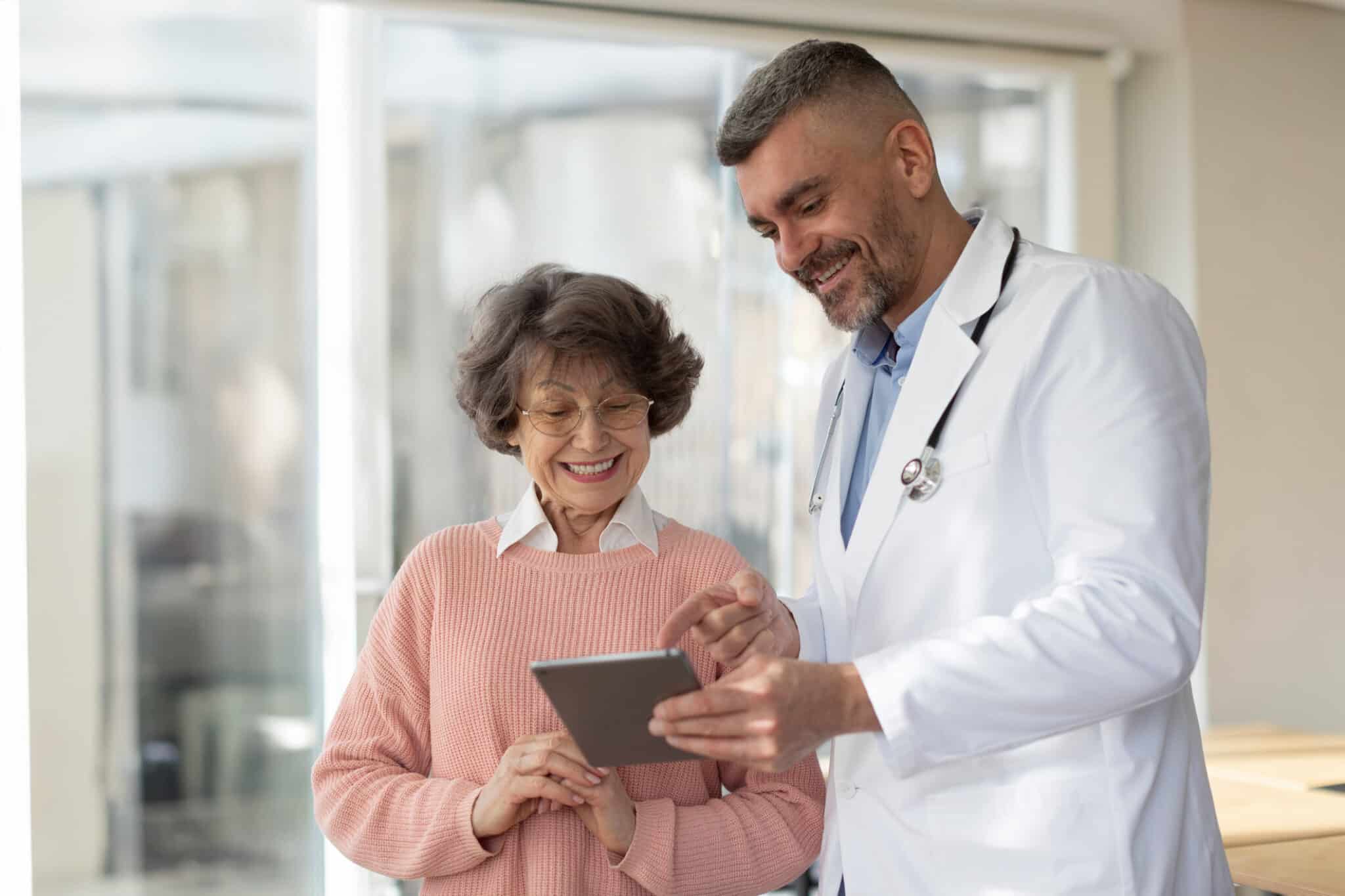 A doctor speaking to an elderly patient while showing something on his tablet