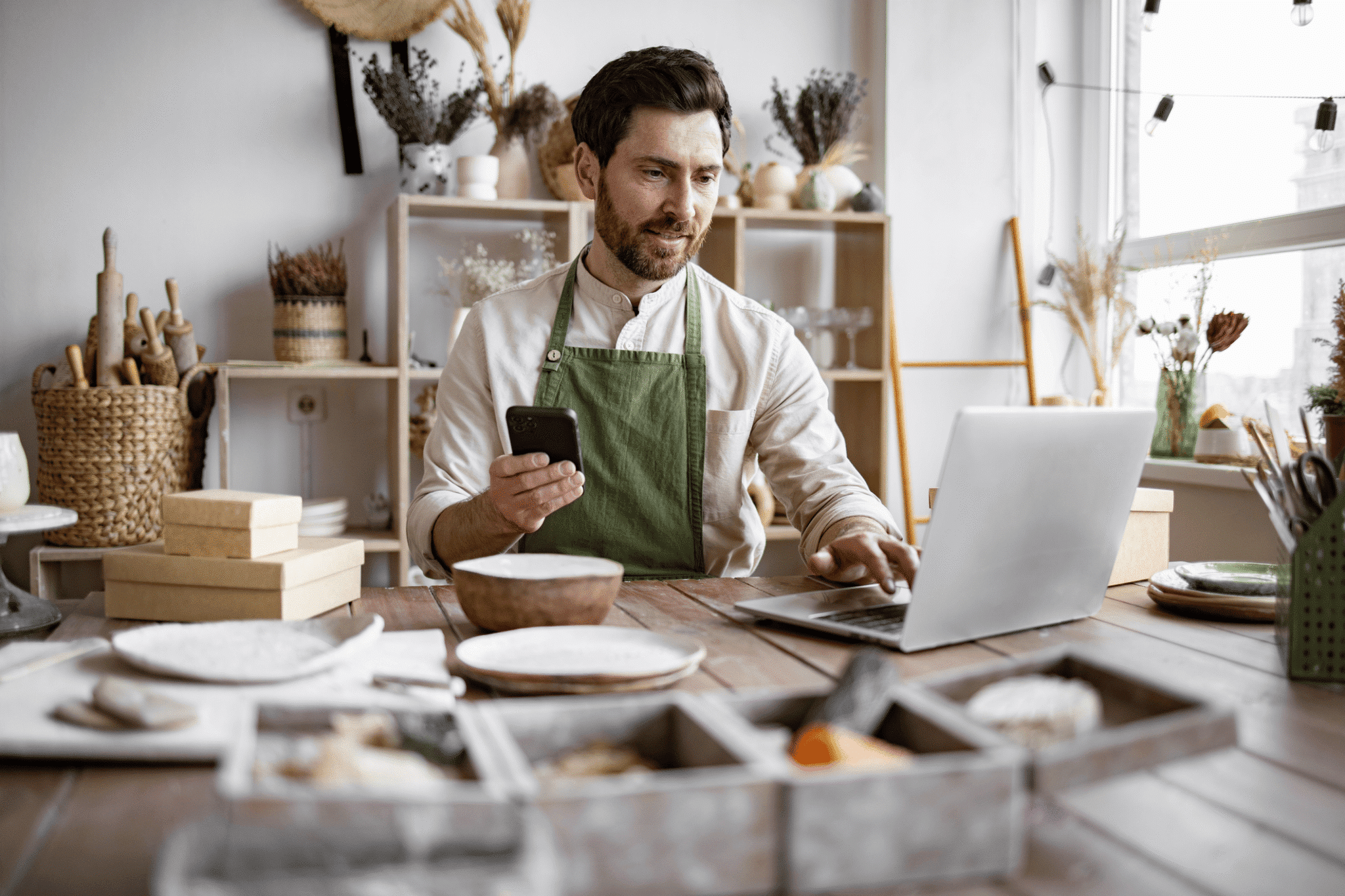 An employee in an arts and craft retail store checks both his laptop and mobile phone