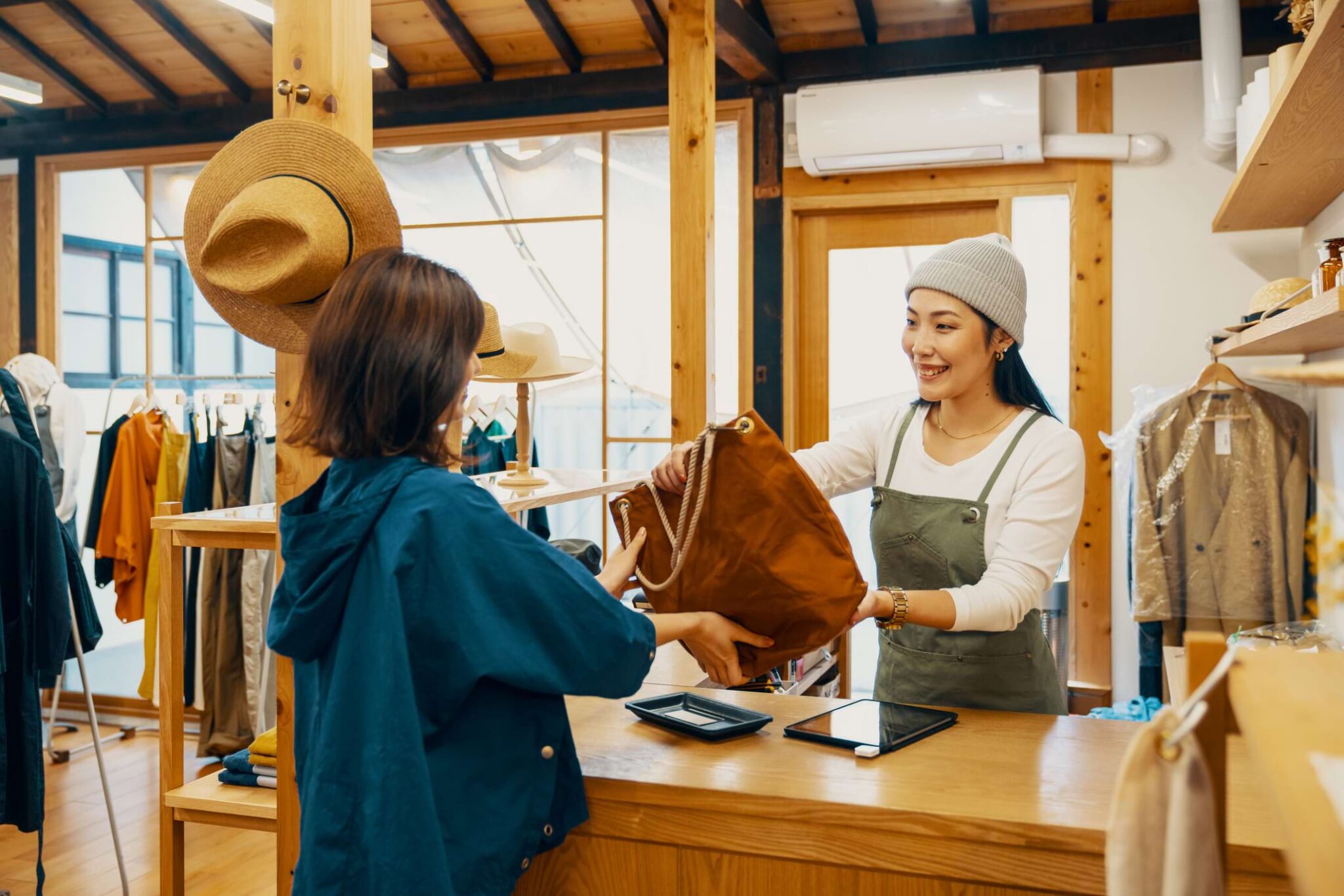 A woman in blue buying a brown bag from a woman in overalls in a rustic retail store
